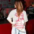 Frau trägt Café NINI Oversized T-Shirt in Creme mit rotem „Go Wild Go NINI Est. 2025" Skater Backprint, Nahaufnahme des Rückenprints im Café NINI
