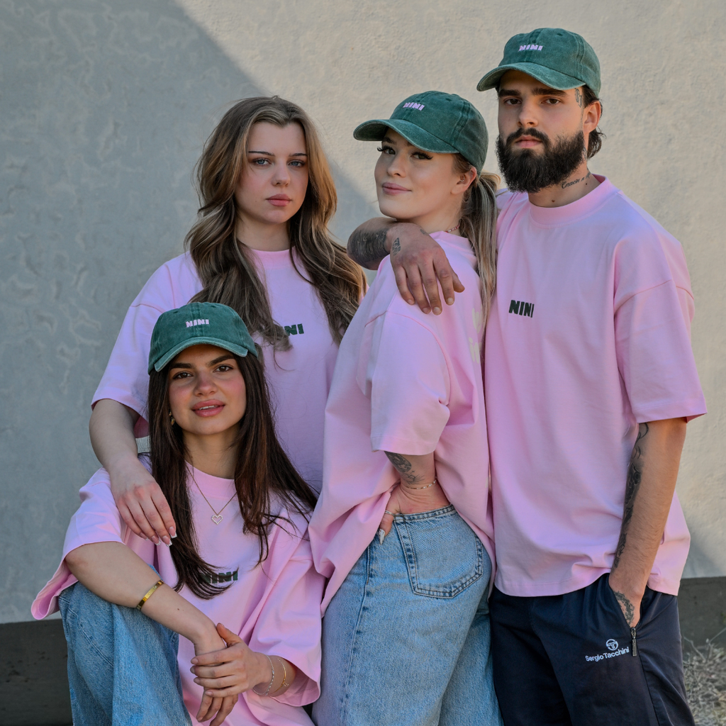Vier Personen tragen Café NINI Oversized T-Shirts in Pink mit NINI Logo und grüne NINI Caps, Gruppen-Lookbook Unisex Merchandise