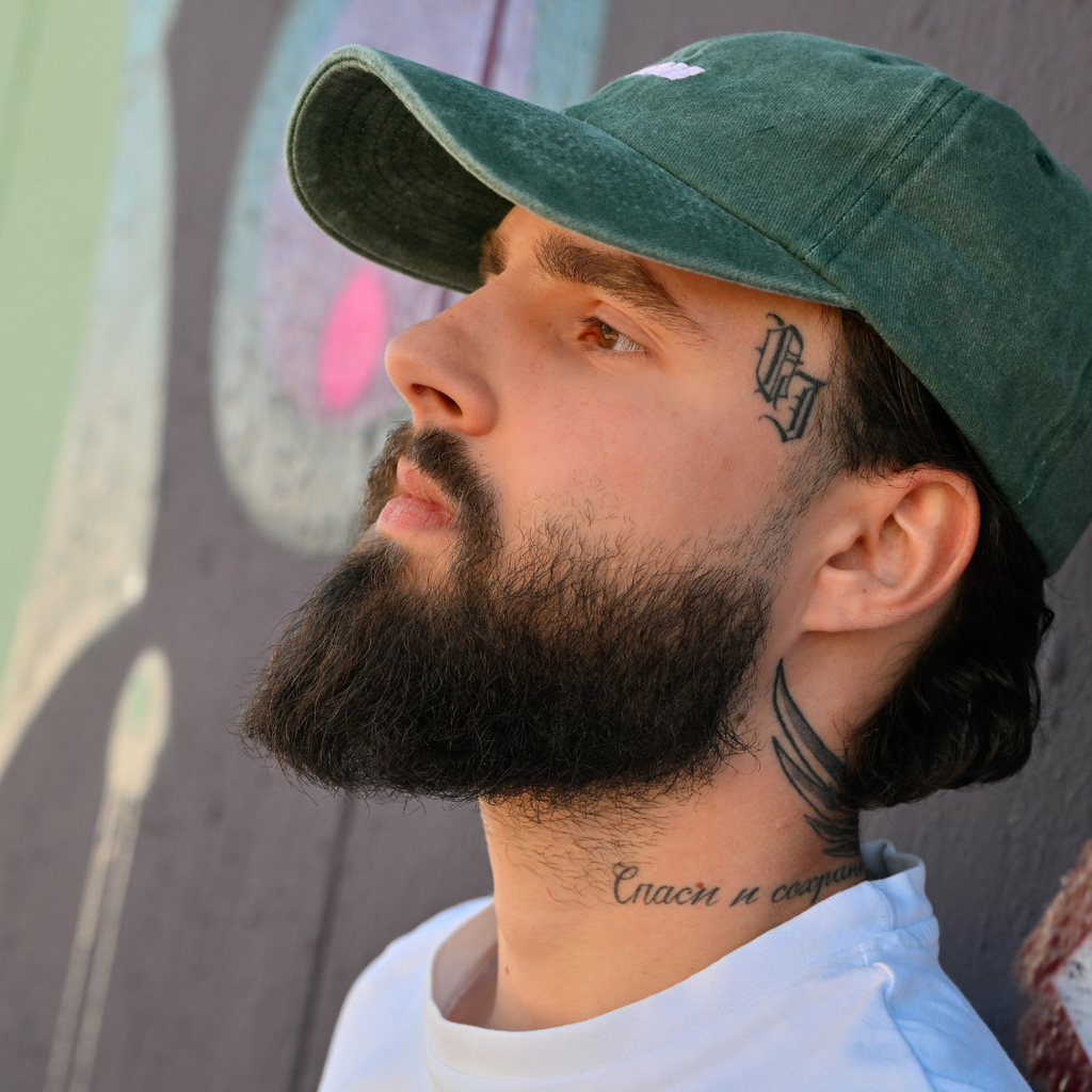 Mann trägt grüne Café NINI Cap im Vintage Wash Look, Seitenansicht vor Graffiti-Wand, lässiges Herren Lifestyle Lookbook