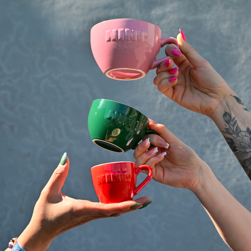 Drei Café NINI Keramik Tassen für Cappuccino, Kaffee und Espresso in Pink, Grün und Rot werden von Händen in die Höhe gehalten, Hochformat Produktbild mit eingeprägtem NINI Logo