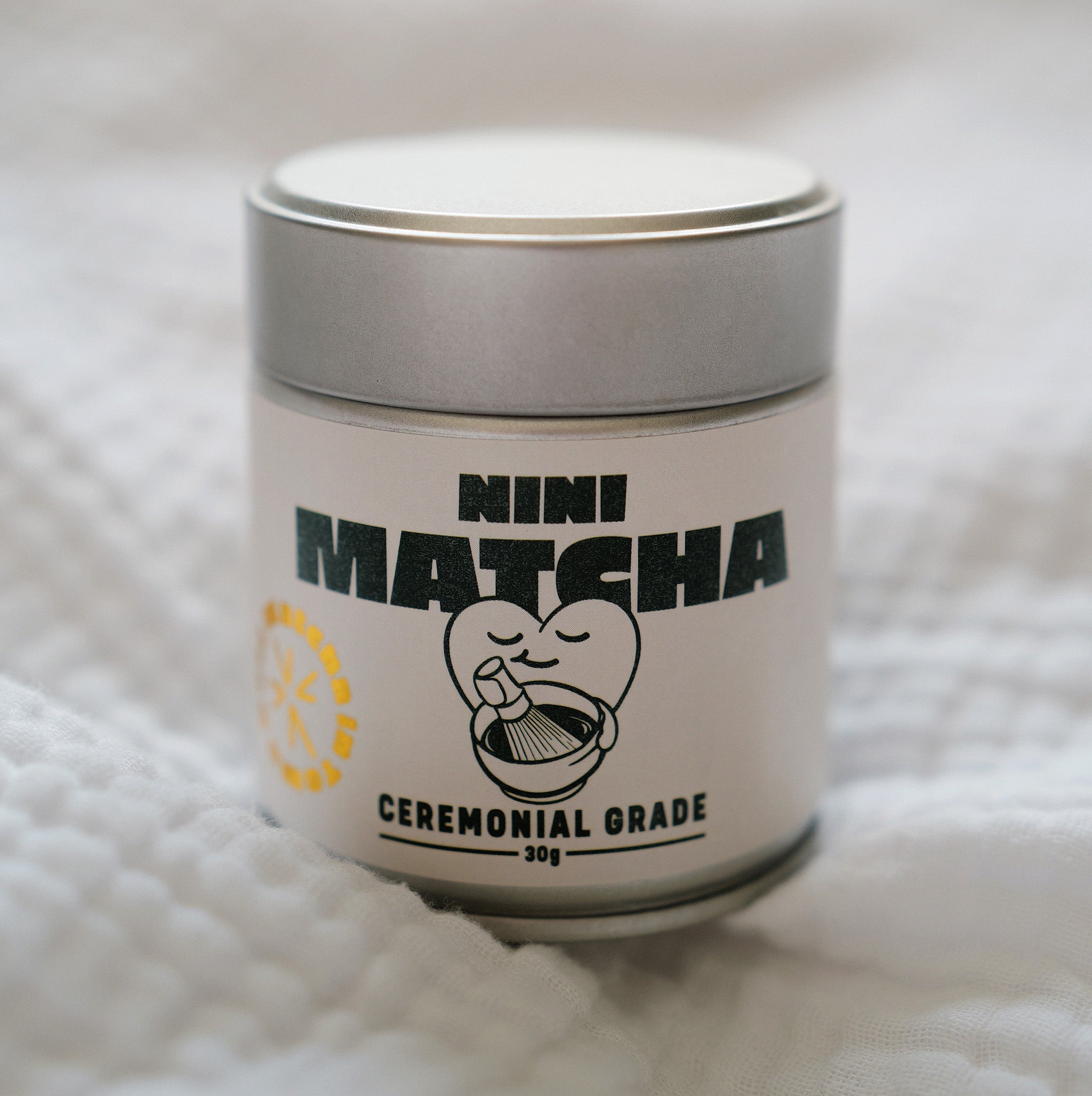Silberne NINI Matcha Dose Ceremonial Grade 30g mit vollständig sichtbarem Etikett und NINI Matcha Logo, frontales Einzelproduktbild auf weißem Stoff