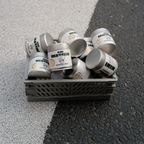 Mehrere silberne NINI Matcha Dosen Ceremonial Grade 30g liegen in einer grauen Transportkiste auf Asphalt, Mengenproduktbild von oben mit sichtbarem NINI Matcha Etikett